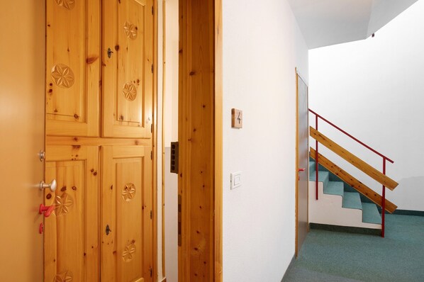 A wooden door with geometric patterns, a staircase with wooden steps and red railings, and a white wall.