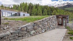 A stone wall leading to a modern building with large windows and a wooden deck. - Apartment 'Larice' with Mountain View, Private Terrace and Shared Garden (Pila)