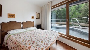 A bedroom with a large window, a bed with floral bedding, and two wooden headboards. - Apartment 'Pino' with Mountain View, Private Terrace and Shared Garden (Pila)