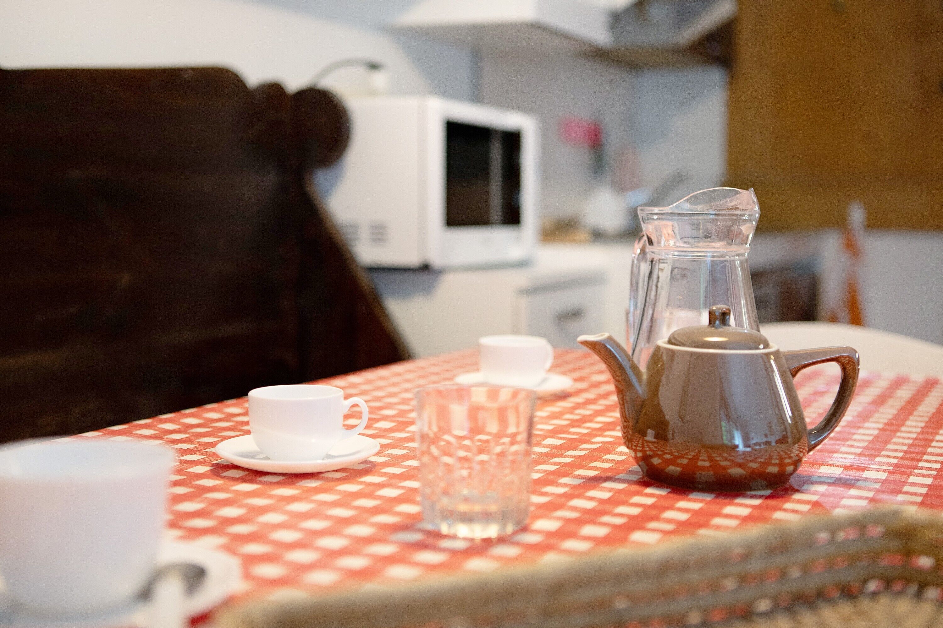 Une table recouverte d’une nappe à carreaux, avec une théière, un pichet en verre et une tasse.