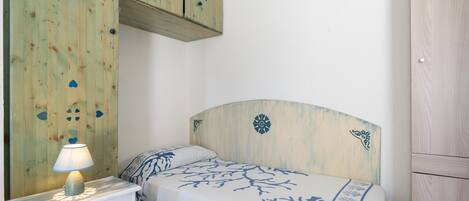 A bedroom with a bed, a nightstand with a lamp, a wooden wardrobe, and a wall with a decorative panel.