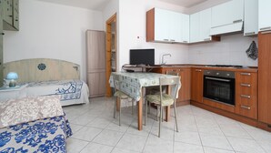 A compact kitchen with a dining table, chairs, a TV, and a ceiling fan.