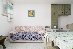 A room with a sofa, a bed, a small table with a lamp, and a cabinet.
