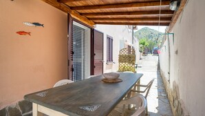 A narrow outdoor corridor with a wooden table and chairs, a metal bowl on the table, and a wooden ceiling.