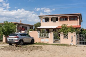 A two-story house with a car parked in front, a gated entrance, and a clear sky.