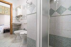 Een badkamer met een douche, twee toiletten, een wastafel en een spiegel.
