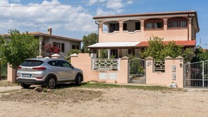 Una casa de dues plantes amb un cotxe davant, una entrada tancada amb reixa i un cel serè.