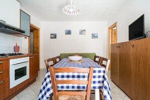 Cozinha com mesa de jantar, cadeiras, fogão, forno e uma televisão sobre um armário.