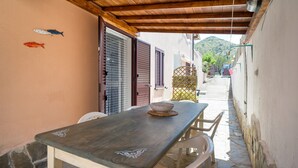 Zona de dinar a l'aire lliure coberta amb taula i cadires, sostre de fusta i vista d'un carrer estret amb edificis i una muntanya al fons.