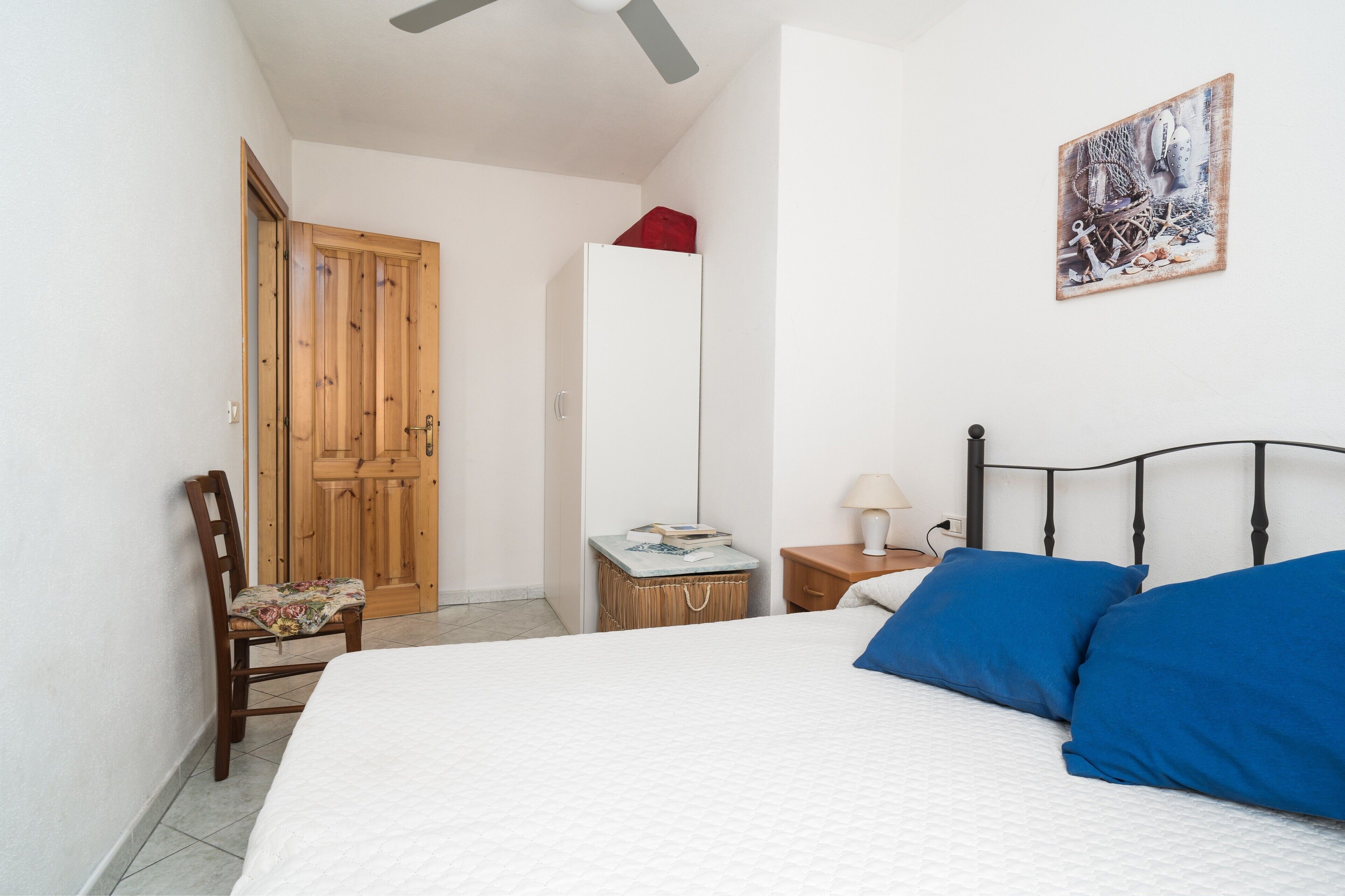 Une chambre à coucher avec un lit, une chaise, une table de chevet, une lampe et une porte.