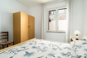 Quarto com cama, guarda-roupa de madeira, cadeira, janela com cortinas e abajur.