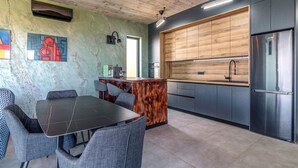 Une cuisine moderne avec des meubles en bois, un réfrigérateur en acier inoxydable et un coin bar équipé d’une machine à café.