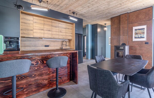 A modern kitchen with wooden cabinets, a built-in oven, and a bar area with stools. - Awesome home in Brovinje (Brovinje)