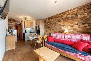 A compact living space with a kitchenette, a sofa with patterned cushions, a wooden table, and a wall with a wooden plank design. - Apartment 'Appartement Aiguille Rouge 420' with Mountain View, Balcony and Wi-Fi (Bourg-Saint-Maurice)