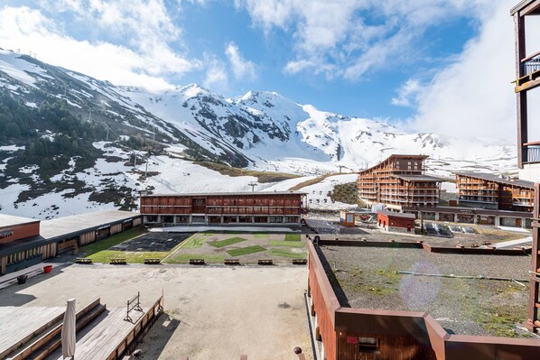 Un paisaje montañoso con picos nevados, un edificio con fachada de madera y un cielo despejado.