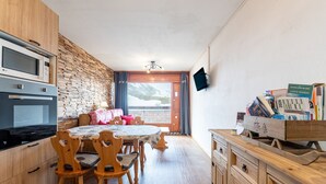 Una cocina compacta con electrodomésticos integrados, un comedor con sillas de madera y vistas a través de una ventana.