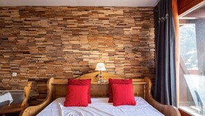 Una cama con cabecera de madera, dos almohadas rojas y una colcha blanca en una habitación con pared de madera.
