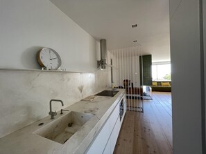 A modern kitchen with a large island, a clock, and a view into a living area with a sofa.