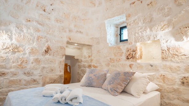 A stone-walled room with a bed, pillows, and a small window. - Villa 'Trullo Bianco Molillo' with Private Garden (Ostuni)