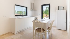 A modern kitchen with white cabinetry, a window, and a dining area with a table and chairs. - Villa 'Trullo Bianco Molillo' with Private Garden (Ostuni)