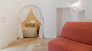 A bedroom with a bed, a red couch, and a white curtain. - Villa 'Trullo Bianco Molillo' with Private Garden (Ostuni)