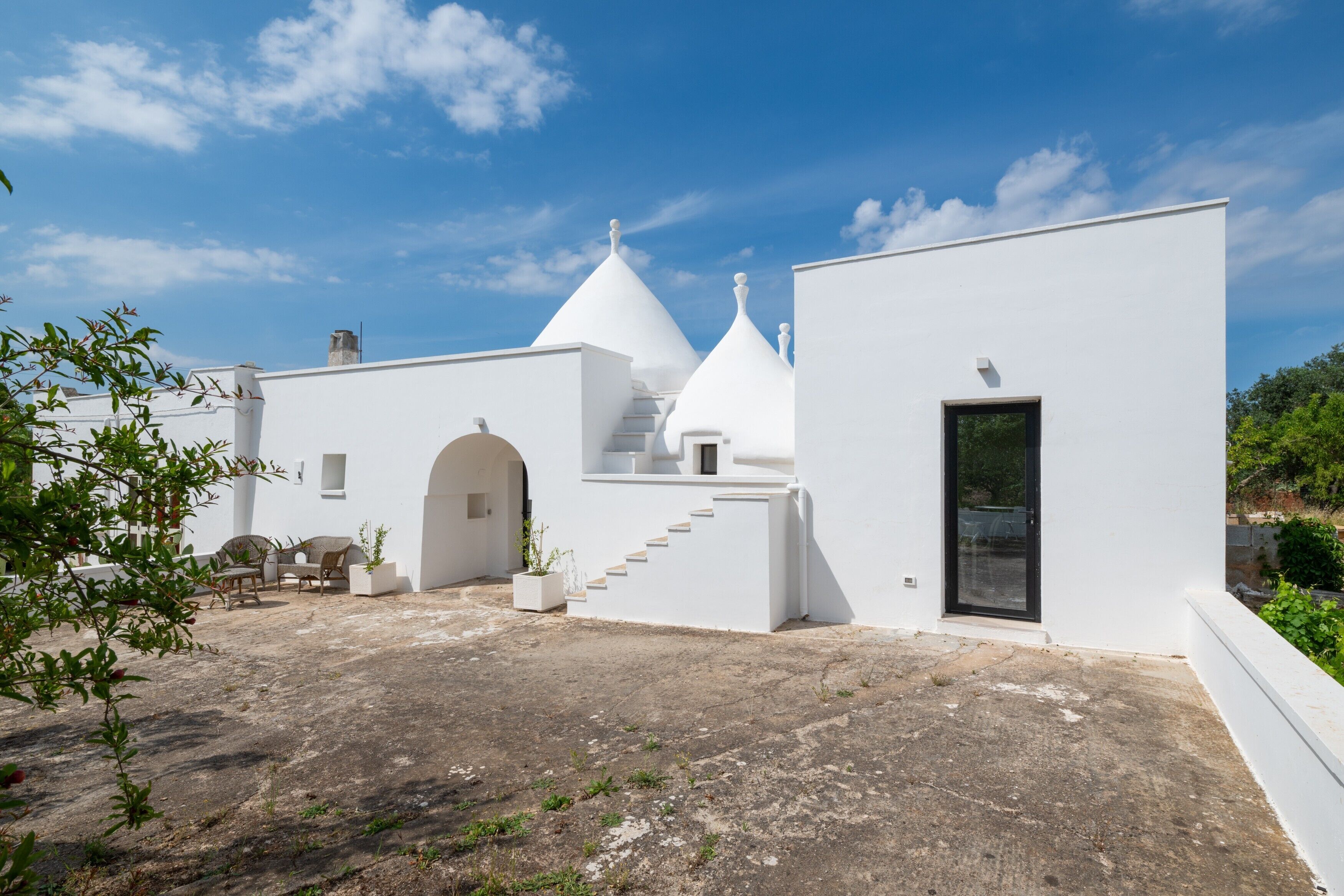 A white building with a black door, a staircase, and a seating area with chairs and a table.