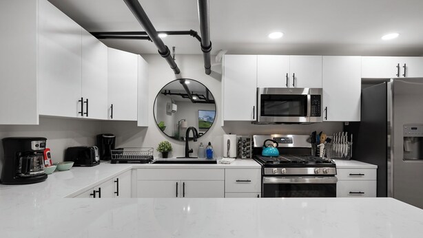 A modern kitchen with white cabinets, stainless steel appliances, a round mirror, and a marble countertop. - Brand NEW Centrally Located with FREE parking and PET friendly!! (Saint Paul)