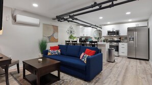 A modern living room with a blue sofa, a wooden coffee table, and a kitchen in the background. - Brand NEW Centrally Located with FREE parking and PET friendly!! (Saint Paul)