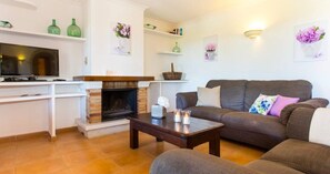 Una sala de estar con chimenea, un sofá, una mesita de centro y un televisor.