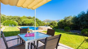 Un patio con una mesa de vidrio, sillas y una piscina.