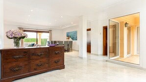 Una habitación amplia con un gran aparador de madera, un área de comedor con sillas, una puerta de cristal que da a otra habitación y un cuadro en la pared.
