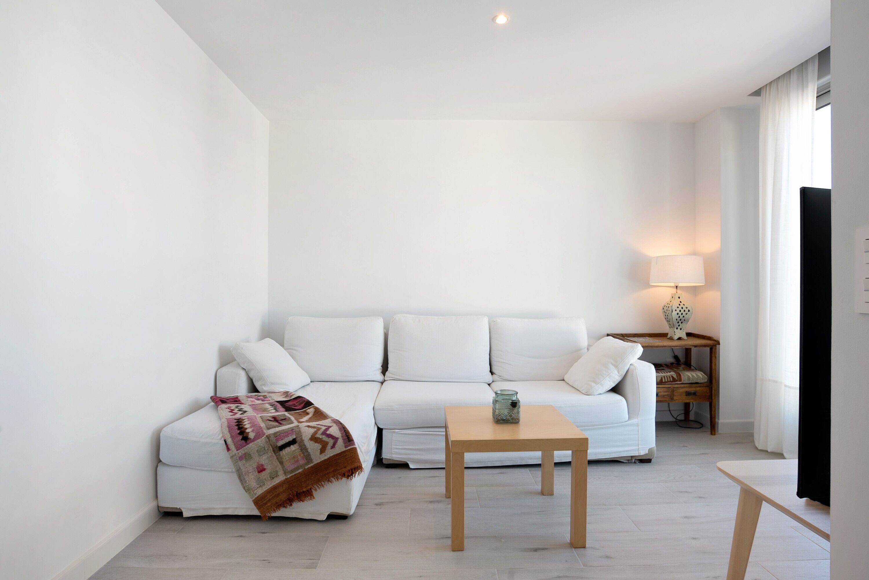 A modern living room with a white sofa, a small wooden table, and a lamp on a side table.
