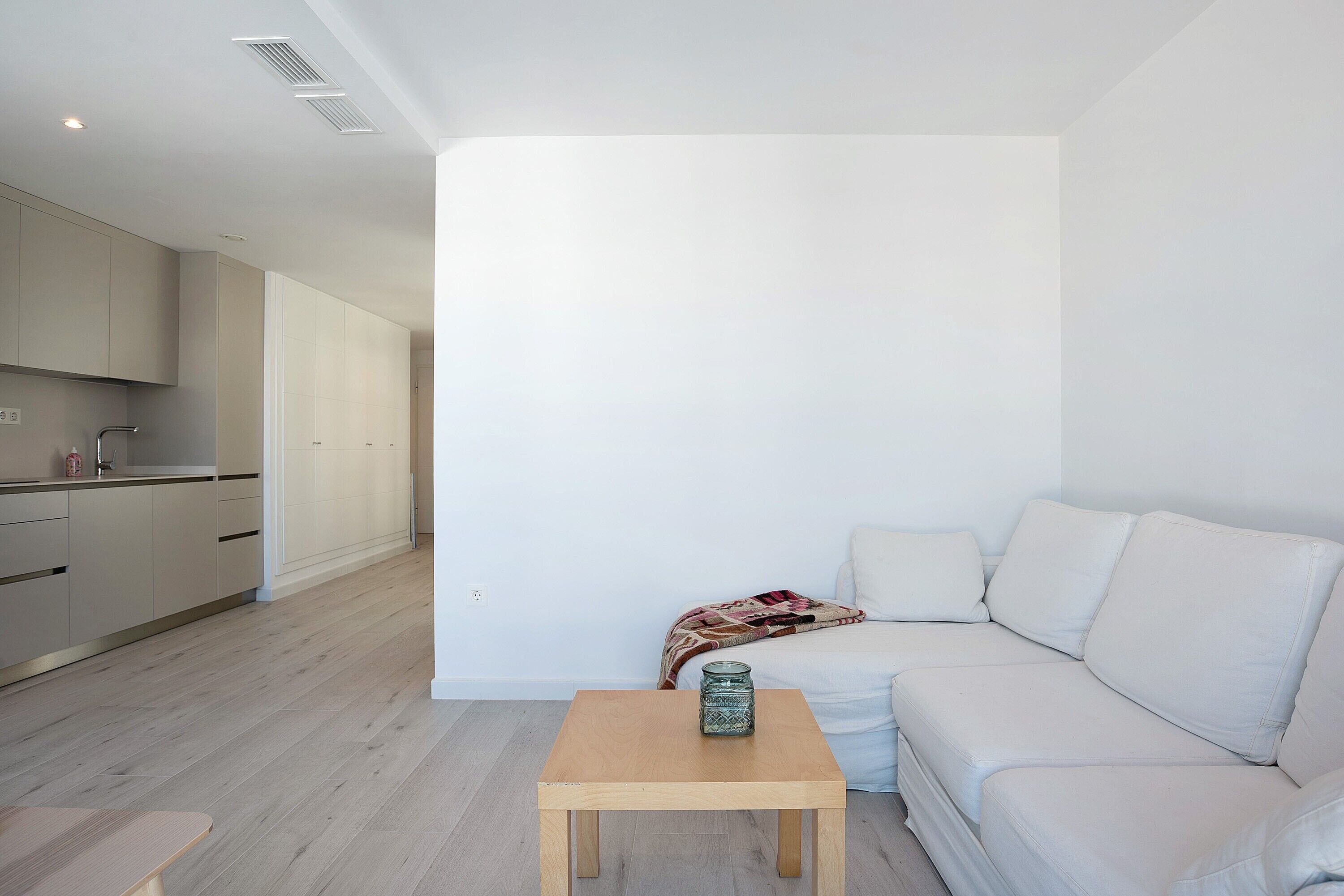 A modern living room with a sofa, a small wooden table, and a kitchen in the background.