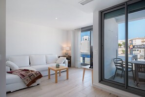Een moderne woonkamer met een witte bank, een klein houten tafeltje en een glazen deur naar een buitenbalkon.