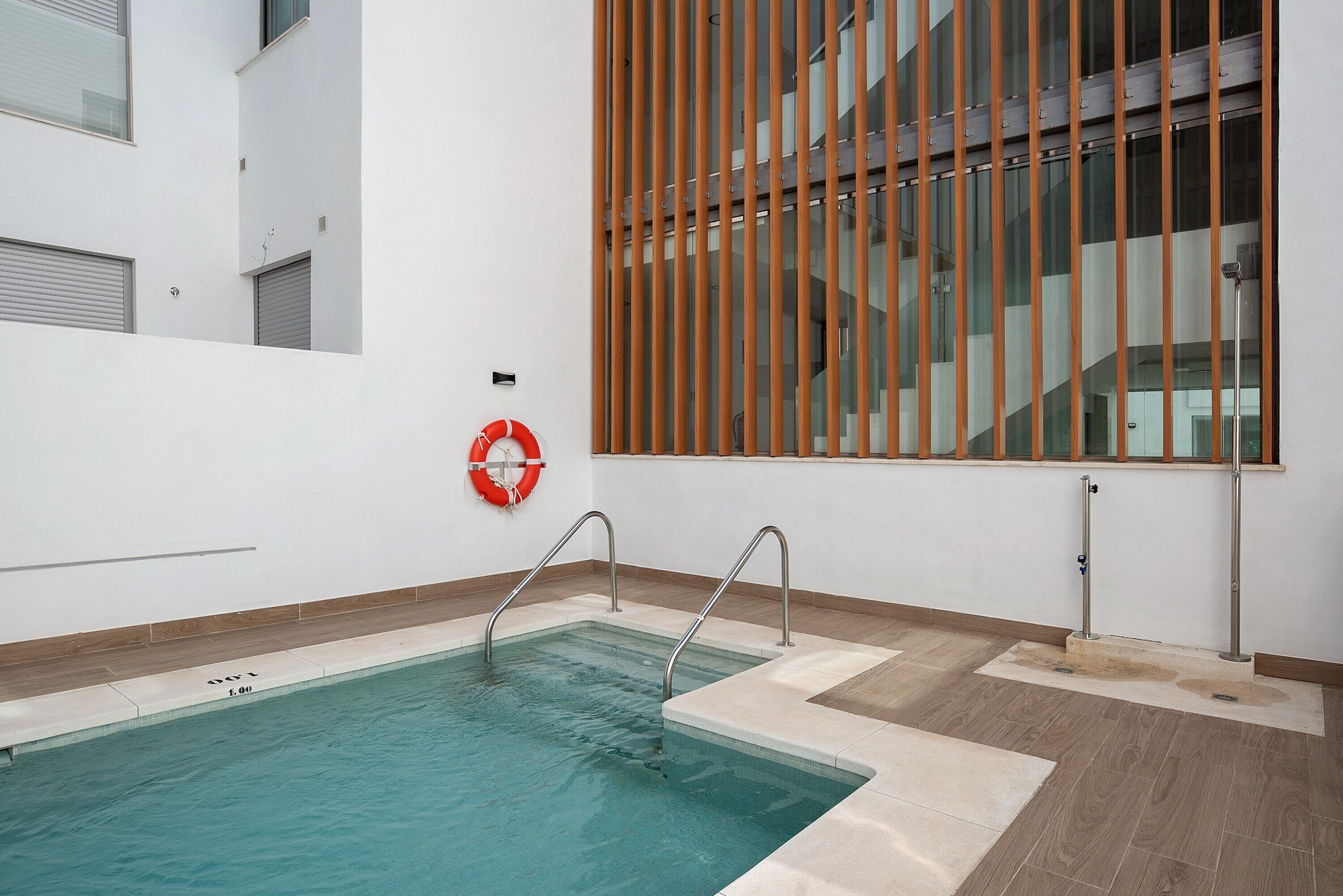 Ein Schwimmbecken mit Metallleitern, einem Rettungsbuhnen und einem Holzjalousie.