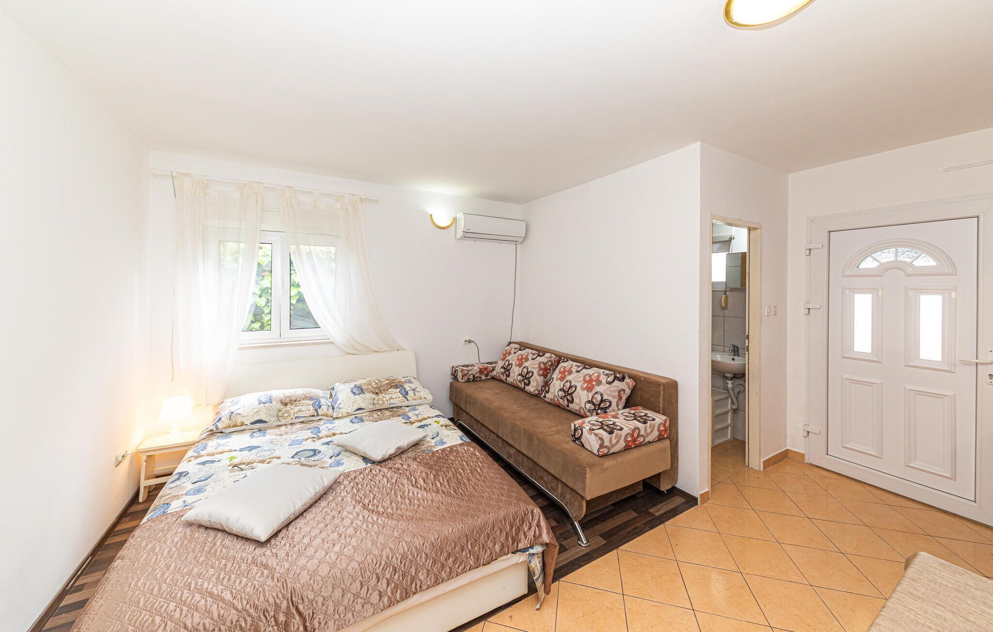 Ein Schlafzimmer mit Bett, Sofa, einem Fenster mit Vorhängen, einer Klimaanlage und einer Tür zu einem Badezimmer.