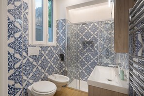 A bathroom with patterned tiles, a toilet, a bidet, a sink, and a window.