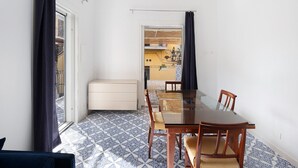 A dining area with a glass table and chairs, a white cabinet, patterned floor tiles, and a view through a door.