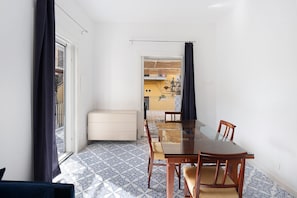 A dining area with a glass table and chairs, a white cabinet, patterned floor tiles, and a view through a door.