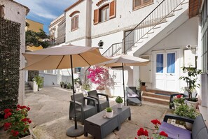 An outdoor seating area with tables and chairs, potted plants, and a staircase leading to an upper floor.