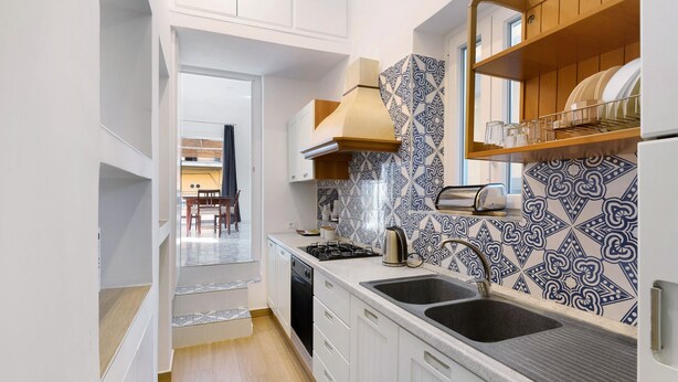 A modern kitchen with white cabinets, a black sink, a stove, and patterned backsplash tiles.