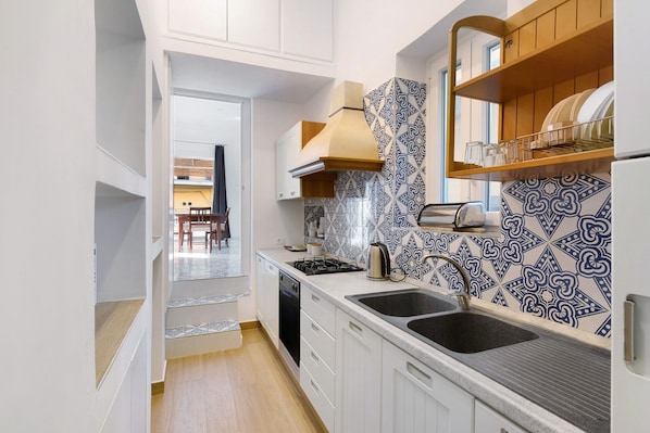 A modern kitchen with white cabinets, a black sink, a stove, and patterned backsplash tiles.