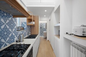 Une petite cuisine étroite, avec une cuisinière à gaz, une bouilloire et un grille-pain posés sur le plan de travail.
