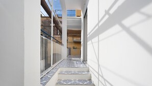 A narrow corridor with patterned tiles, a metal railing, and a view of a building with balconies.