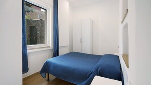 A bedroom with a bed, a window with curtains, a wardrobe, and a small table.