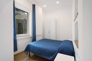 A bedroom with a bed, a window with curtains, a wardrobe, and a small table.