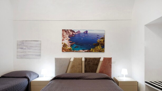 A bedroom with two beds, a nightstand with a lamp, and a painting of a coastal landscape.
