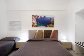 A bedroom with two beds, a nightstand with a lamp, and a painting of a coastal landscape.