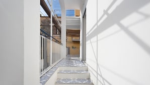 A narrow corridor with patterned tiles, a metal railing, and a view of a building with balconies.