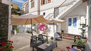 An outdoor seating area with tables and chairs, potted plants, and a staircase leading to an upper floor.